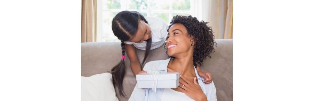 pretty-mother-sitting-on-couch-with-daughter-offering-a-gift-picture-id817290382