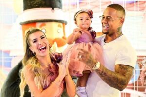 Bebe usando vestido rosa, perto do pai e mãe