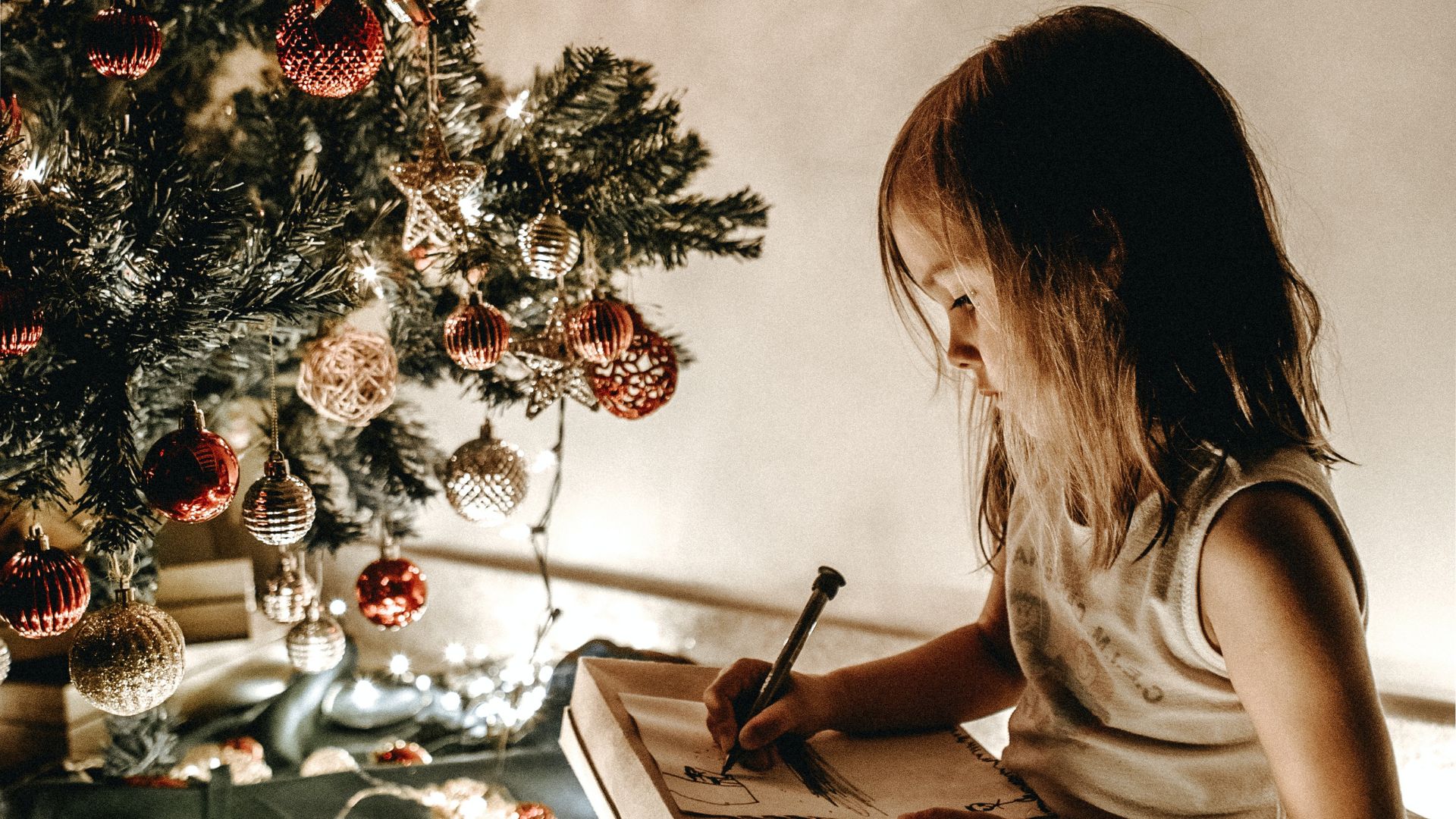 Menina escrevendo carta para o Papai Noel em cen&aacute;rio natalino