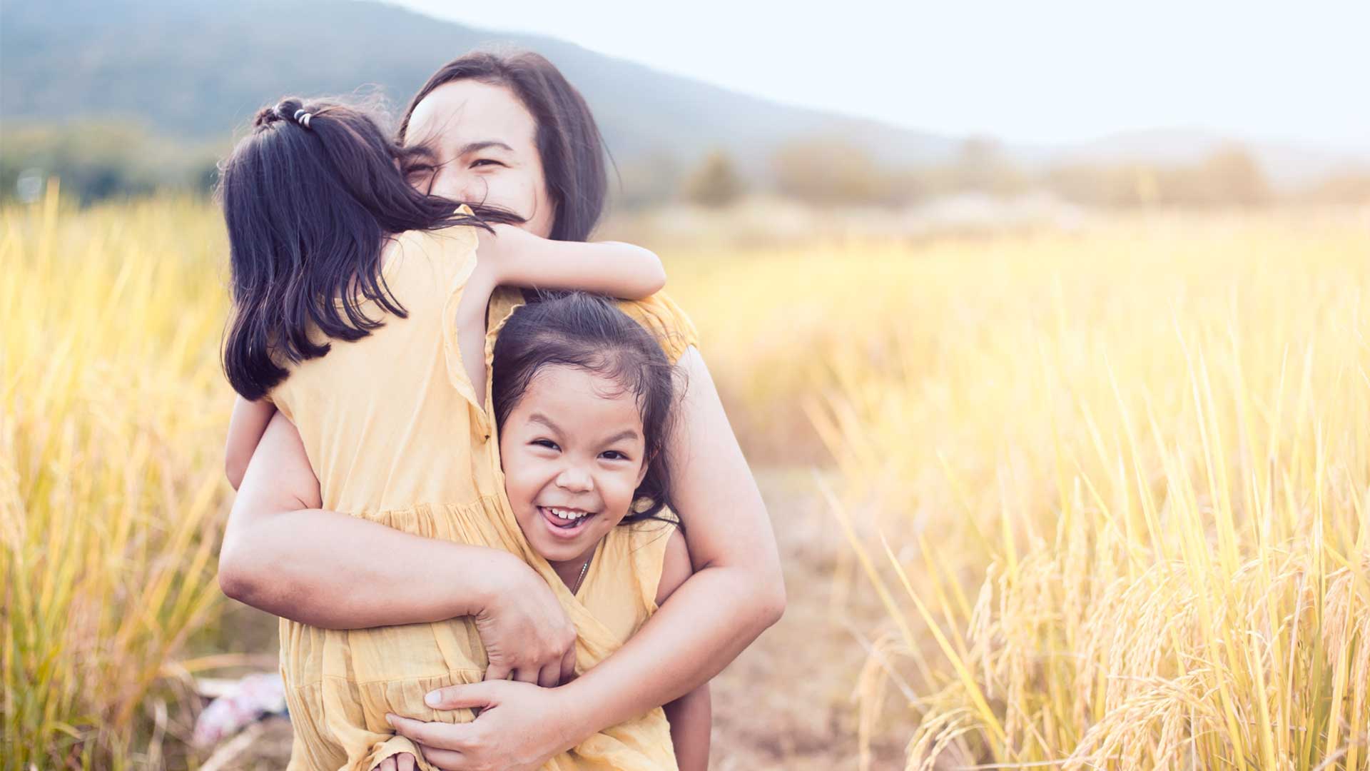 m&atilde;e abra&ccedil;ando duas filhas em campo