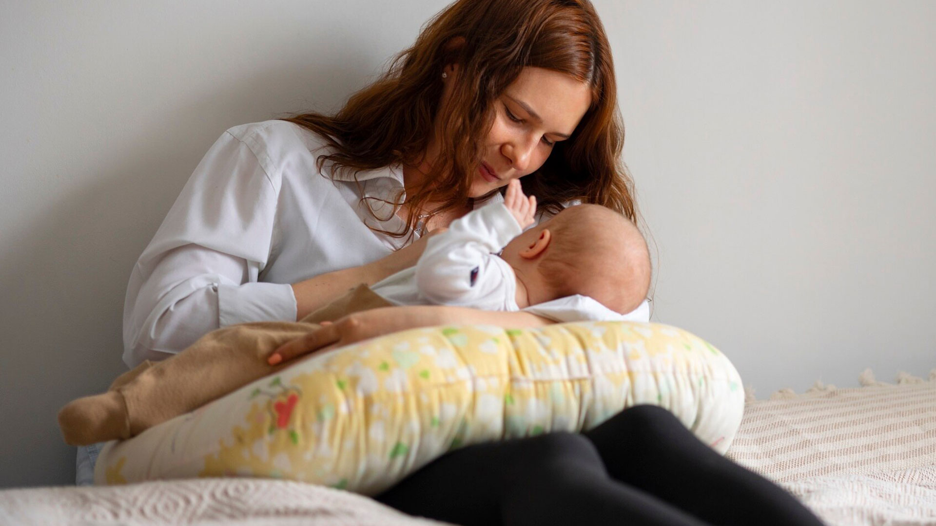 mulher sentada na cama amamentando beb&ecirc; 
