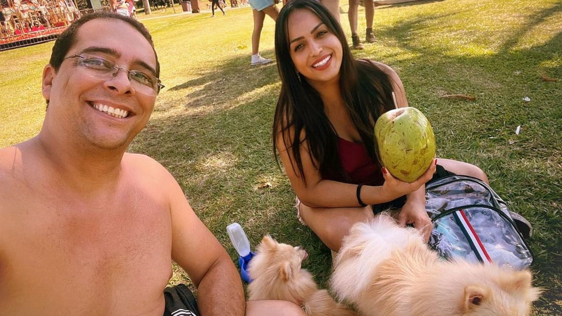 Casal em um parque tomando &aacute;gua de coco com cachorros