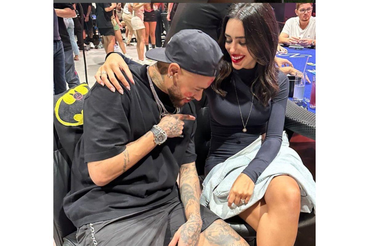 Casal Neymar e Bruna sorrindo enquanto Neymar aponta para a barriga de sua namorada.