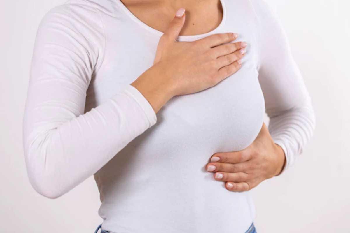 Câncer de mama, prevenção ao câncer de mama, outubro rosa, mulher com as mãos no seio, mulher fazendo auto exame de câncer de mama