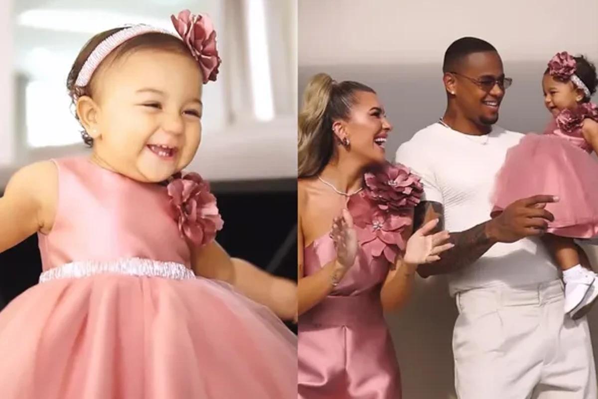 Bebe usando vestido rosa, perto do pai e mãe