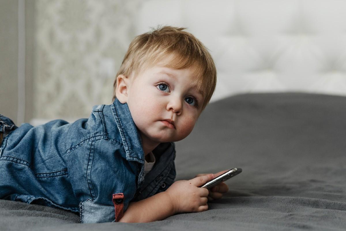 Bebê menino deitado com celular na mão