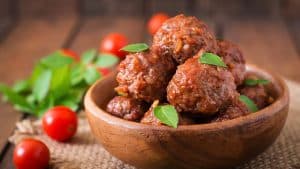 Almôndega ao molho de tomate em uma tigela de madeira com tomate cereja atrás.