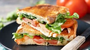 Sanduíche de frango, pão de forma, tomate, queijo e salada em primeiro plano.