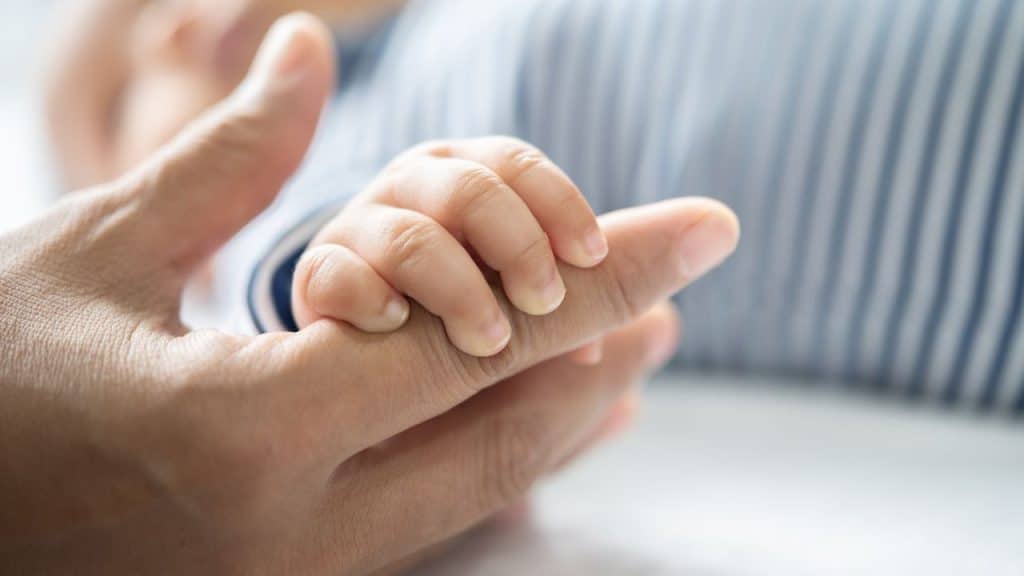 Bebê segura a mão da mãe, simbolizando a adoção.