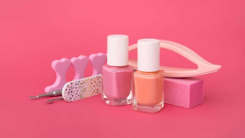 Esmaltes e utensílios de unha em fundo rosa.
