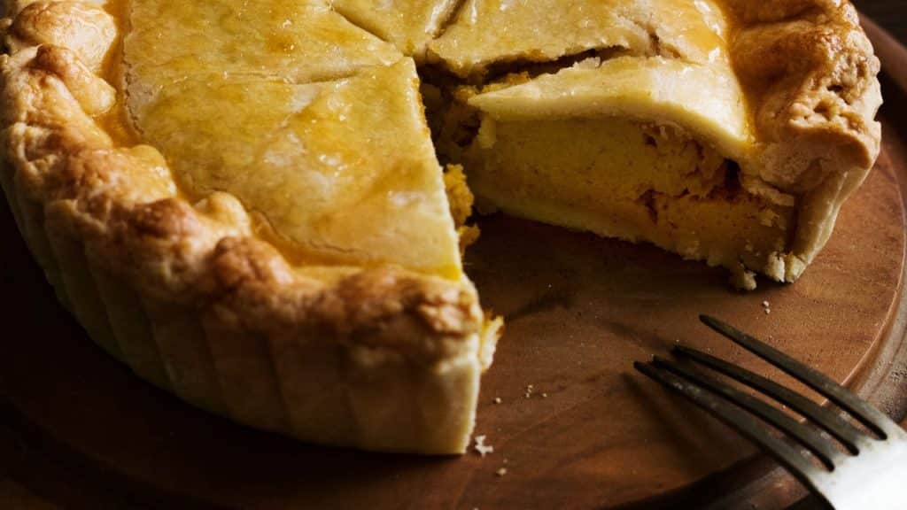 Empadão de frango em bandeja de madeira com garfo.