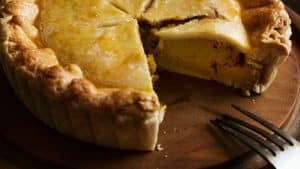 Empadão de frango em bandeja de madeira com garfo.