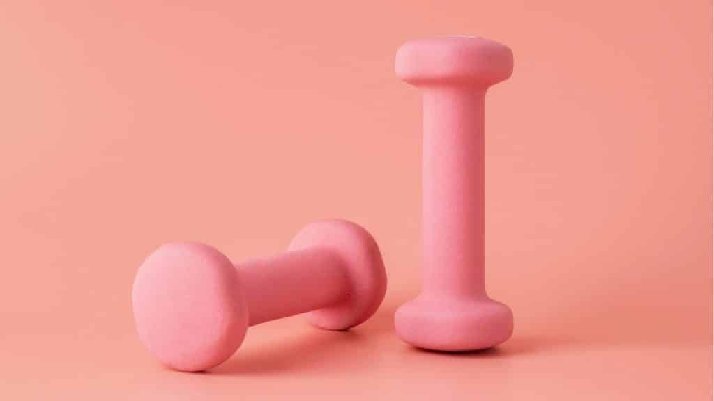 Dois pesos rosados de exercícios em um fundo da mesma cor.
