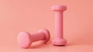 Dois pesos rosados de exercícios em um fundo da mesma cor.