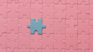 Peça azul se destacando em um quebra-cabeça rosa, representando a brincadeira de uma criança autista.