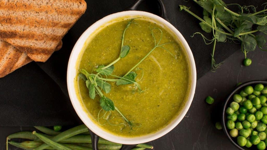 Caldo verde em bancada preta acompanhado de pão e vegetais.