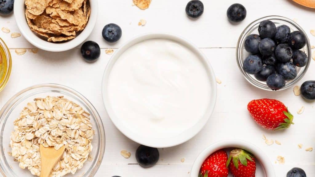Pote de iogurte caseiro natural em meio a frutas e acompanhamentos.