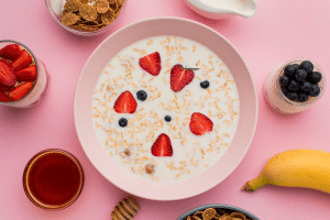 Prato com iogurte e outras frutas em volta, em um fundo cor de rosa.