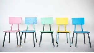 Cadeiras coloridas dispostas em fila representando brincadeiras antigas.