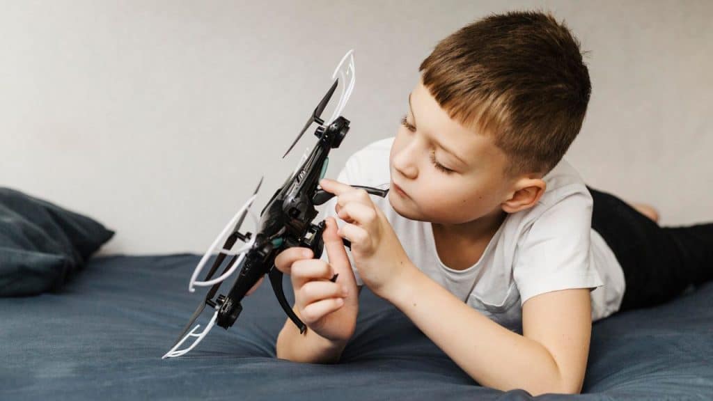 Menino deitado em uma cama aprendendo a usar drones.