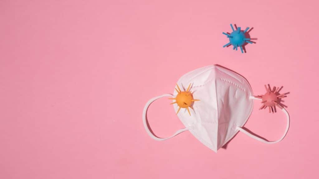 Máscara com vírus coloridos em fundo rosa, representando a dor de garganta.