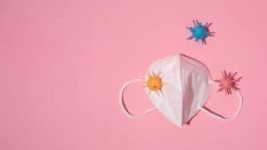 Máscara com vírus coloridos em fundo rosa, representando a dor de garganta.