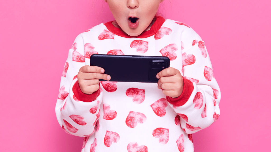 Criança com celular na mão e um pijama rosa e branco