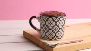 Brownie em uma caneca em cima de uma tábua de madeira com fundo rosa.