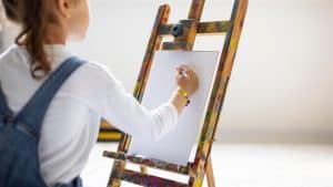 Criança pintando sua obra de arte em uma tela no cavalete.