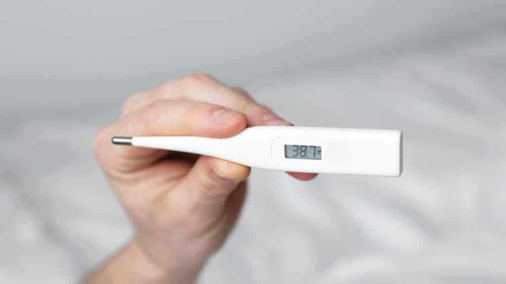Pessoa segurando um termômetro que indica febre.