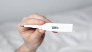 Pessoa segurando um termômetro que indica febre.