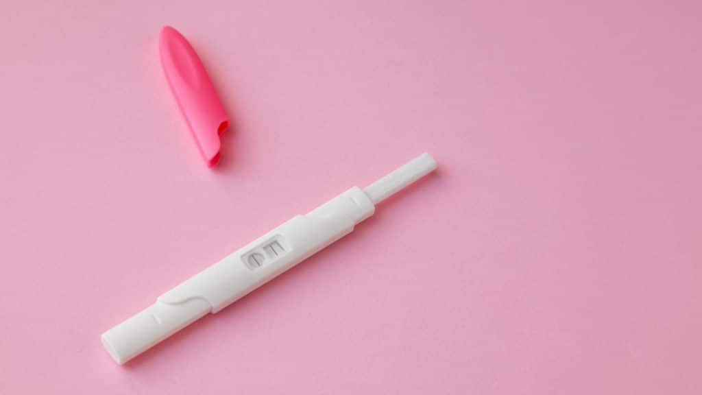 Teste de gravidez com tampa rosa em um fundo rosa claro.