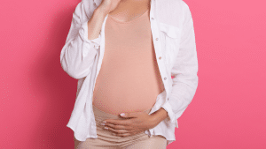 Uma barriga de uma mulher grávida, A mão dela está segurando a barriga. O fundo da imagem é rosa