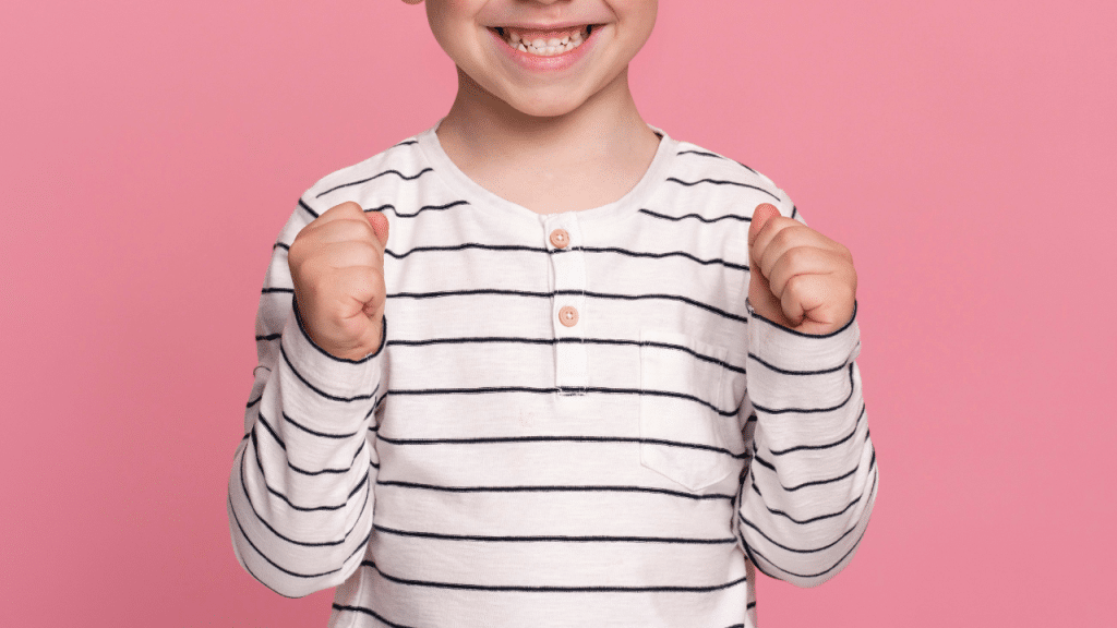 Sorrios de uma criança (menino), com uma camisa listrada e um fundo rosa