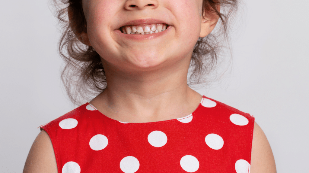 Criança sorrindo com um vestido de bolinhas brancas e vermelho