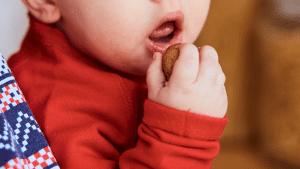 Bebê colocando um alimento na boca, o que parece ser um biscoito