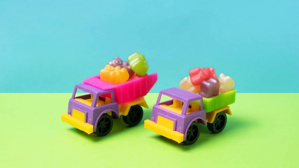 Brinquedos de caminhões coloridos com gomas em cima em um fundo azul e verde.