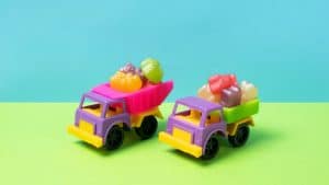 Brinquedos de caminhões coloridos com gomas em cima em um fundo azul e verde.