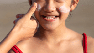 Menina sorrindo com uma mão passando protetor solar