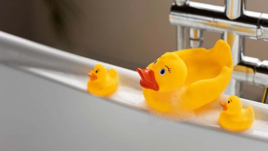 3 patos de borracha na beira de uma banheira representando o banho das crianças.