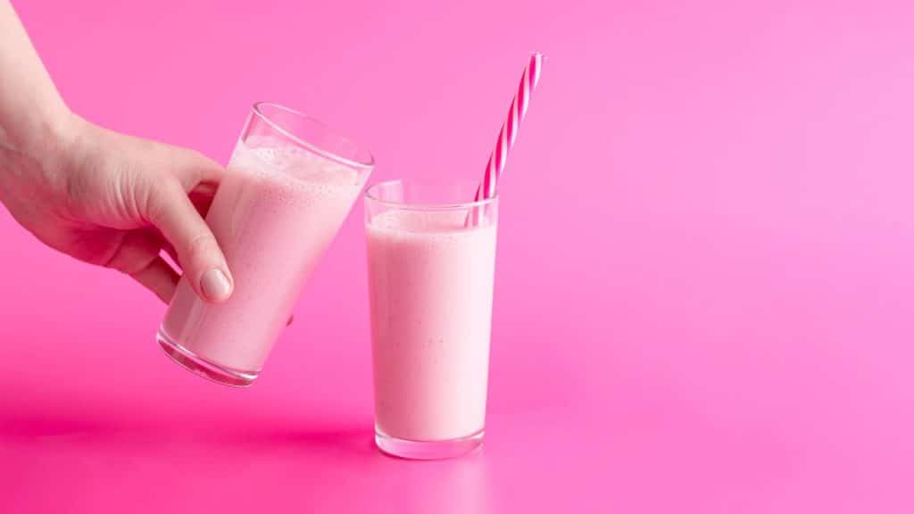 Dois copos de Nesquik natural ao lado de uma mão em um fundo rosa.