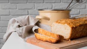 Pão de micro-ondas em cima de uma tábua de madeira com uma panela e uma parede de tijolos brancos atrás.