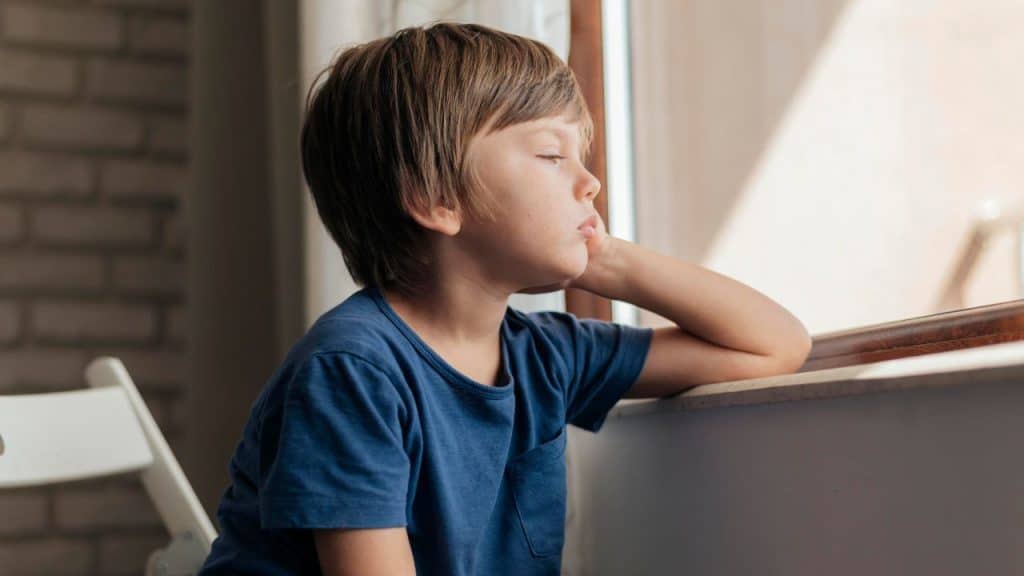 Menino entediado olhando pela janela.