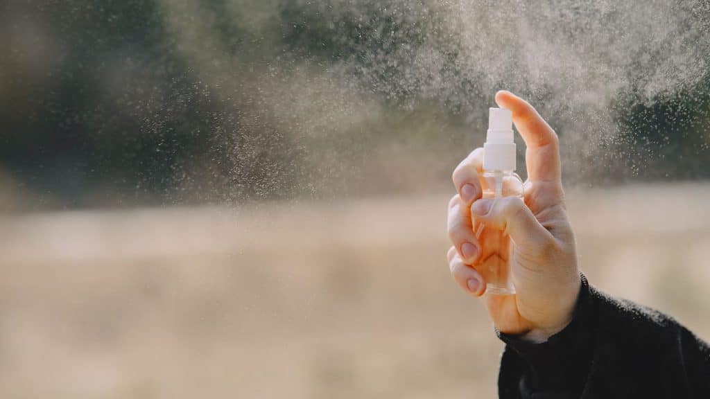 Pessoa espirrando repelente de insetos no ar.