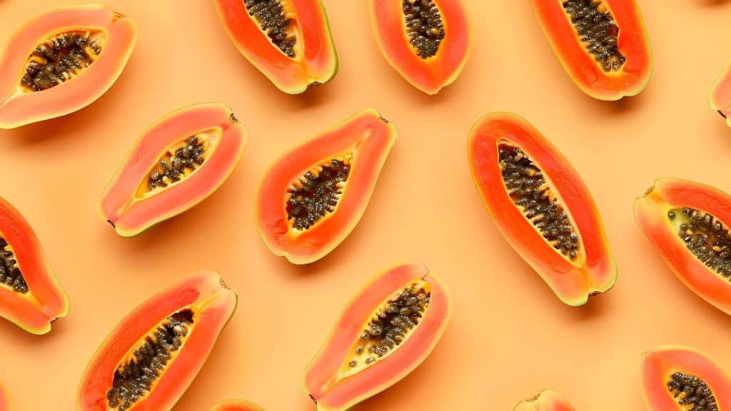 Várias unidades cortadas de mamão espalhadas em um fundo laranja claro.