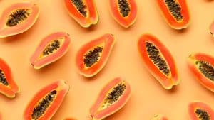 Várias unidades cortadas de mamão espalhadas em um fundo laranja claro.