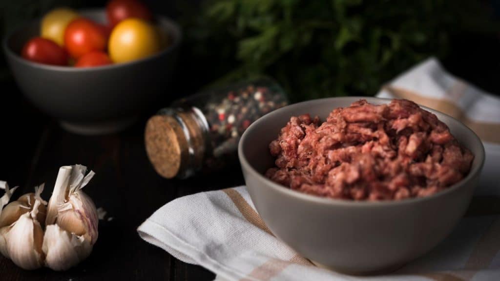 Carne moída em uma tigela com alho e vegetais atrás.