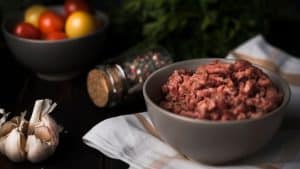 Carne moída em uma tigela com alho e vegetais atrás.