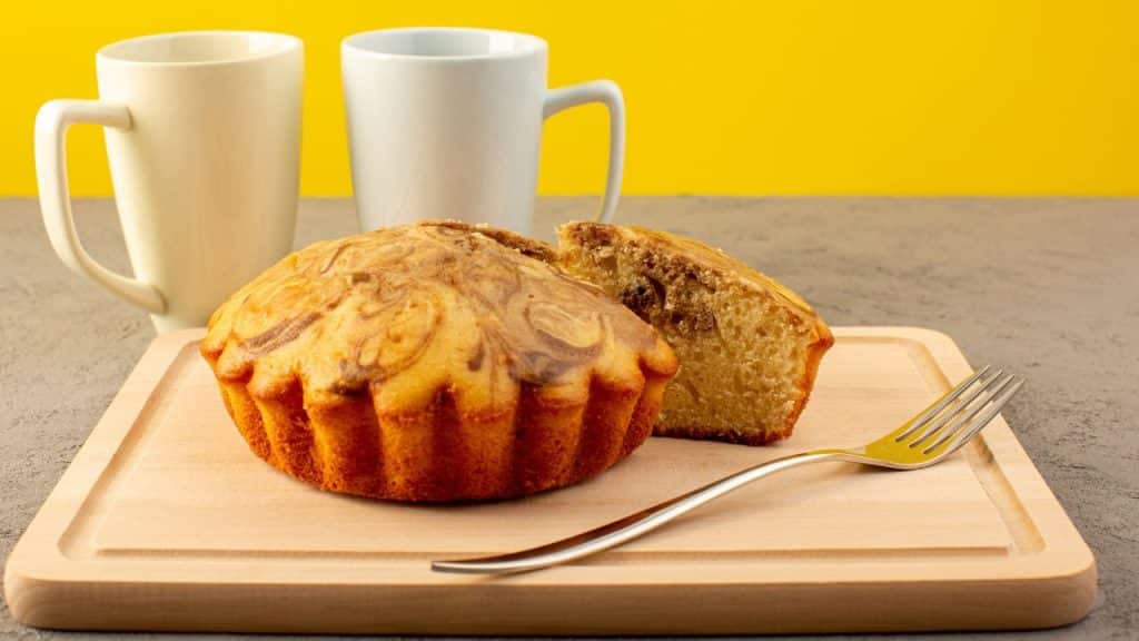 Bolo de caneca fit em uma tábua de madeira ao lado de duas xícaras em um fundo amarelo.
