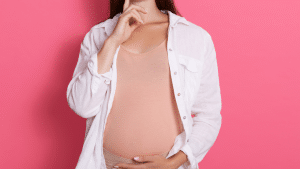 Mulher grávida com a mão na barriga, a imagem está em um fundo rosa.